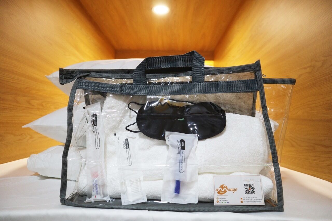 A clear plastic bag containing a black face mask, white tissues, and a small bottle, likely containing hand sanitizer, placed on a white surface.
