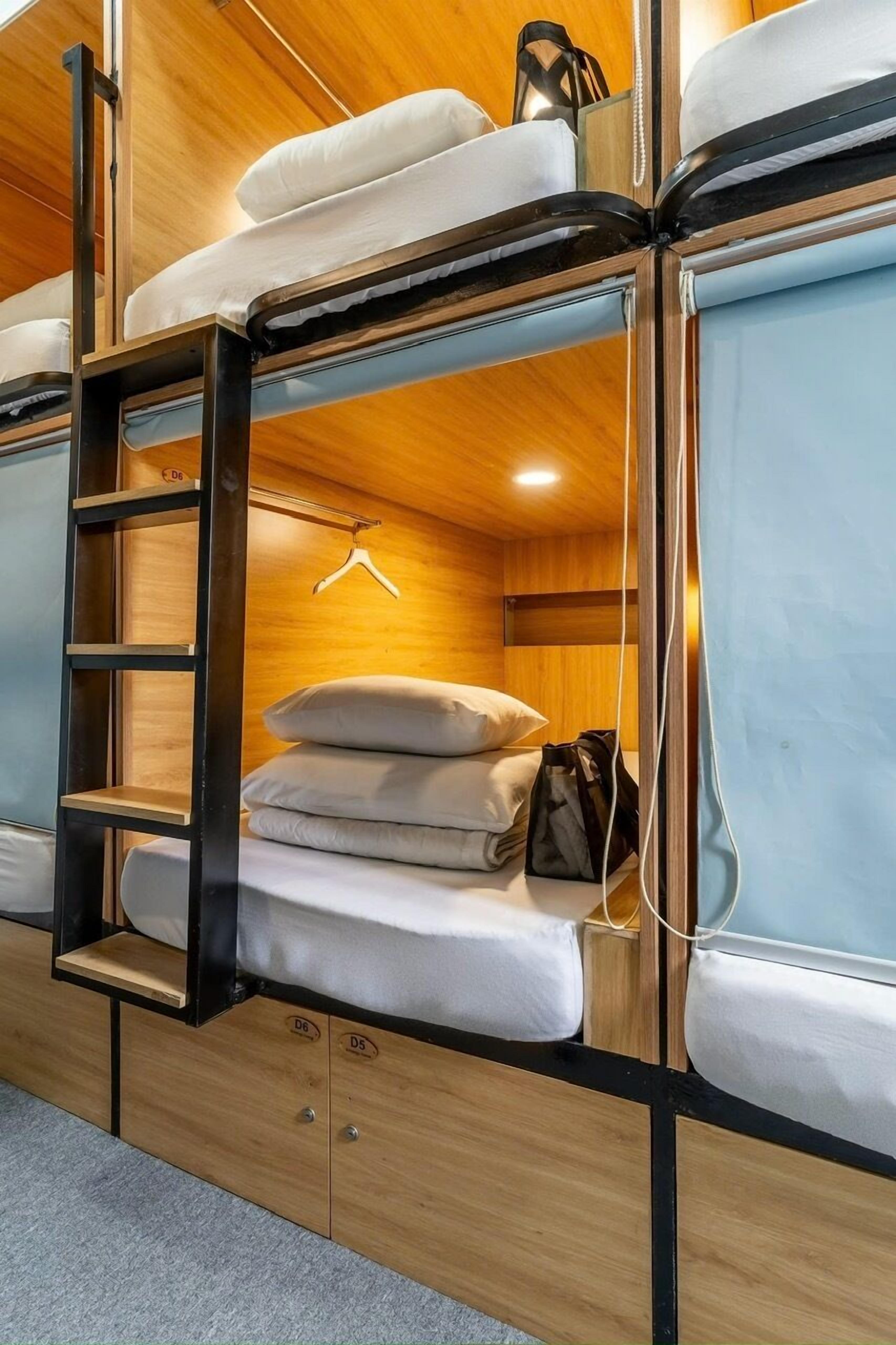 Een stapelbed met een houten trap en opbergladen, een hanglamp en een klein plankje.