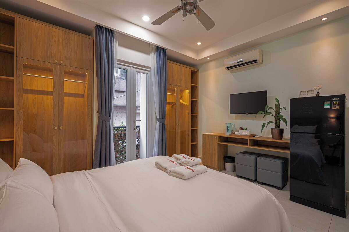 A hotel room with a bed, wardrobe, desk, TV, and refrigerator.