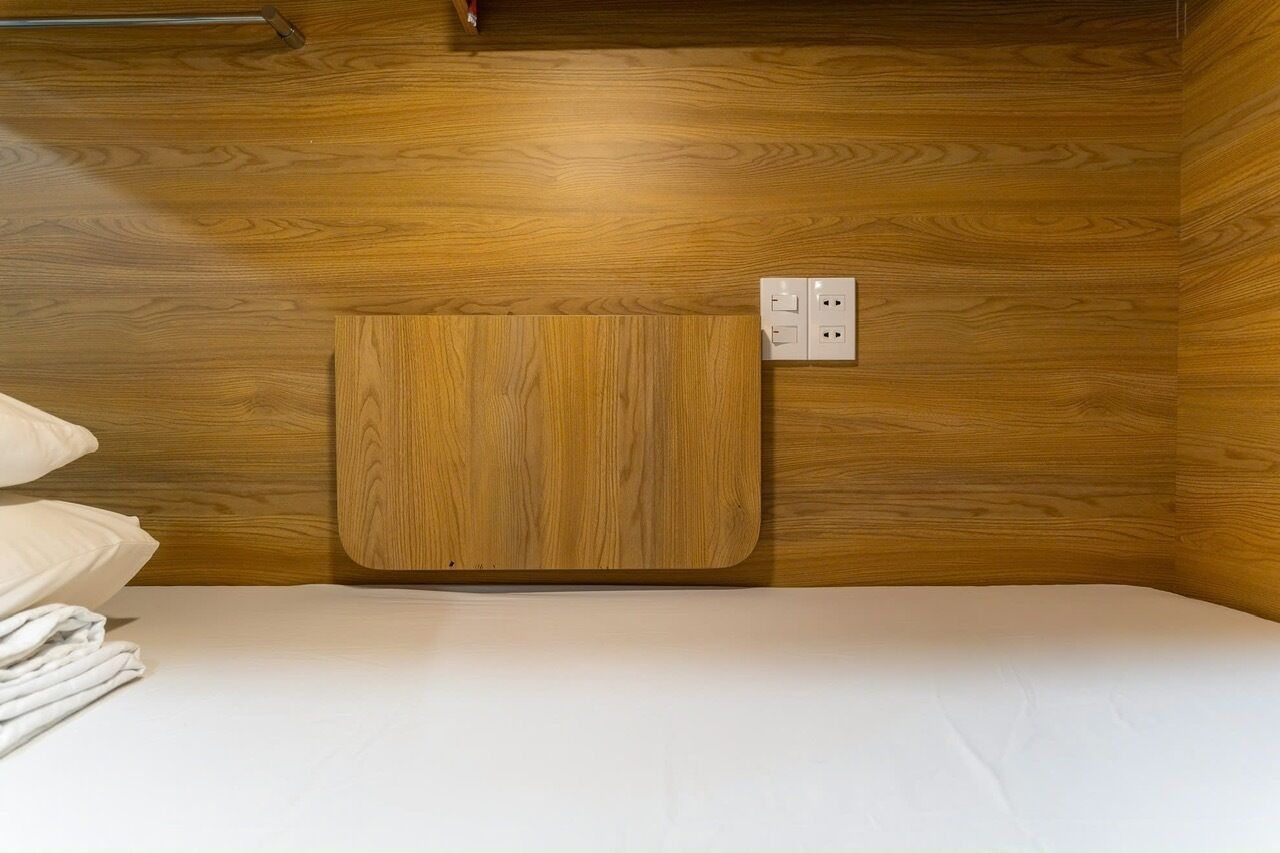 A wooden-paneled room with a bed, a small wooden cabinet, and a power outlet on the wall.