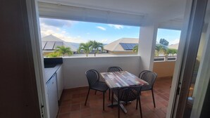 Ein Balkon mit Tisch und Stühlen, Blick auf Gebäude und Palmen, und ein gefliester Boden.