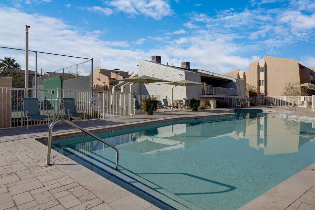 A swimming pool with a metal ladder, lounge chairs, and a covered seating area.