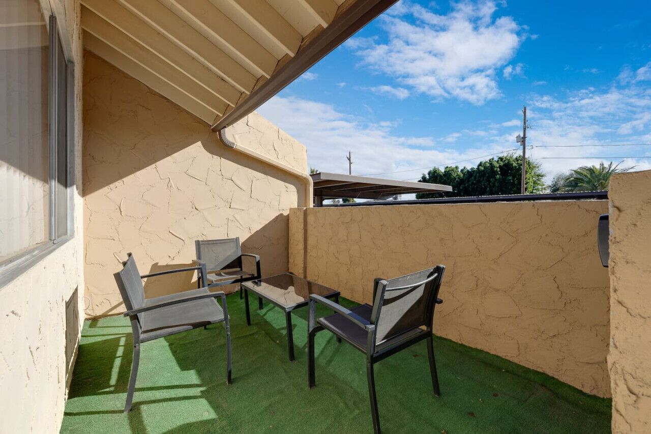 Ein Balkon mit einem Belag aus grünem Kunstrasen, beigen Wänden und Metallstühlen.