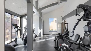 Uma academia moderna com diversos equipamentos de exercício, grandes janelas e um ventilador de teto.
