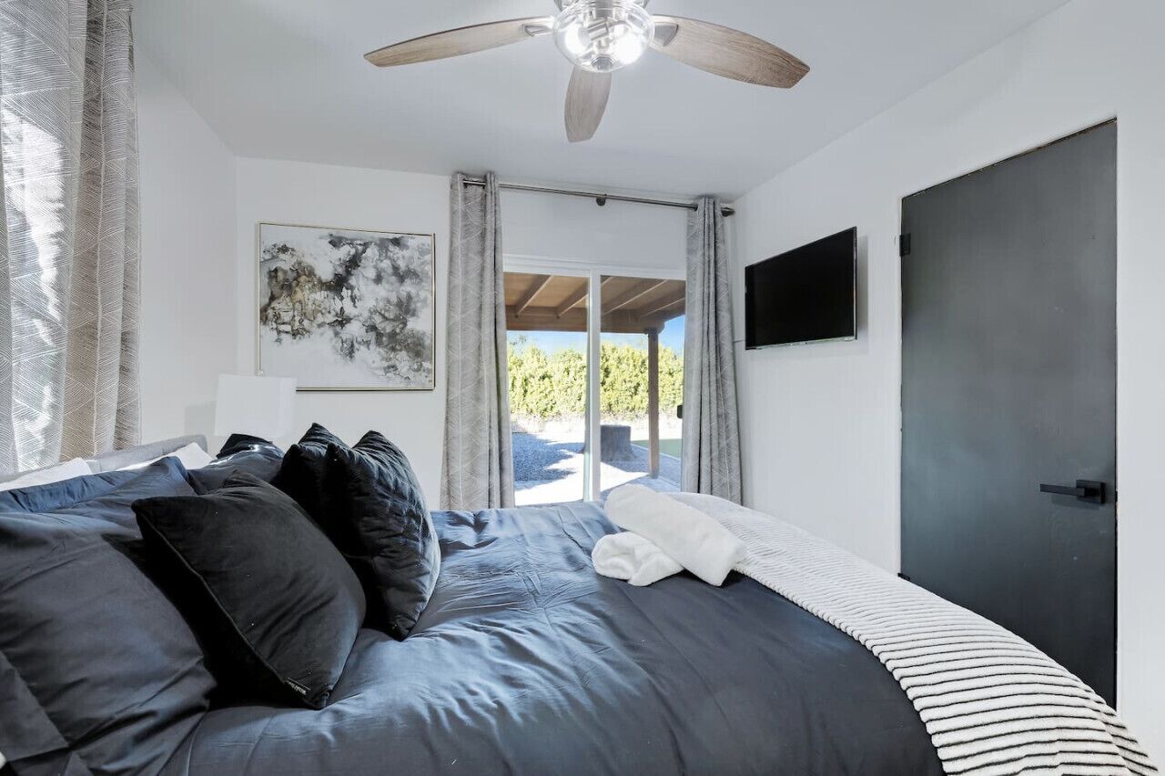 A bedroom with a bed, a ceiling fan, a TV, and a door leading to an outdoor area.