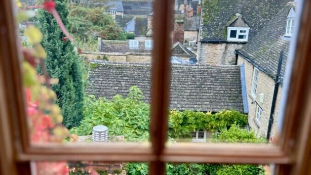 Vista a través de una ventana que muestra una zona residencial con una torre destacada, casas de ladrillo y zonas verdes.