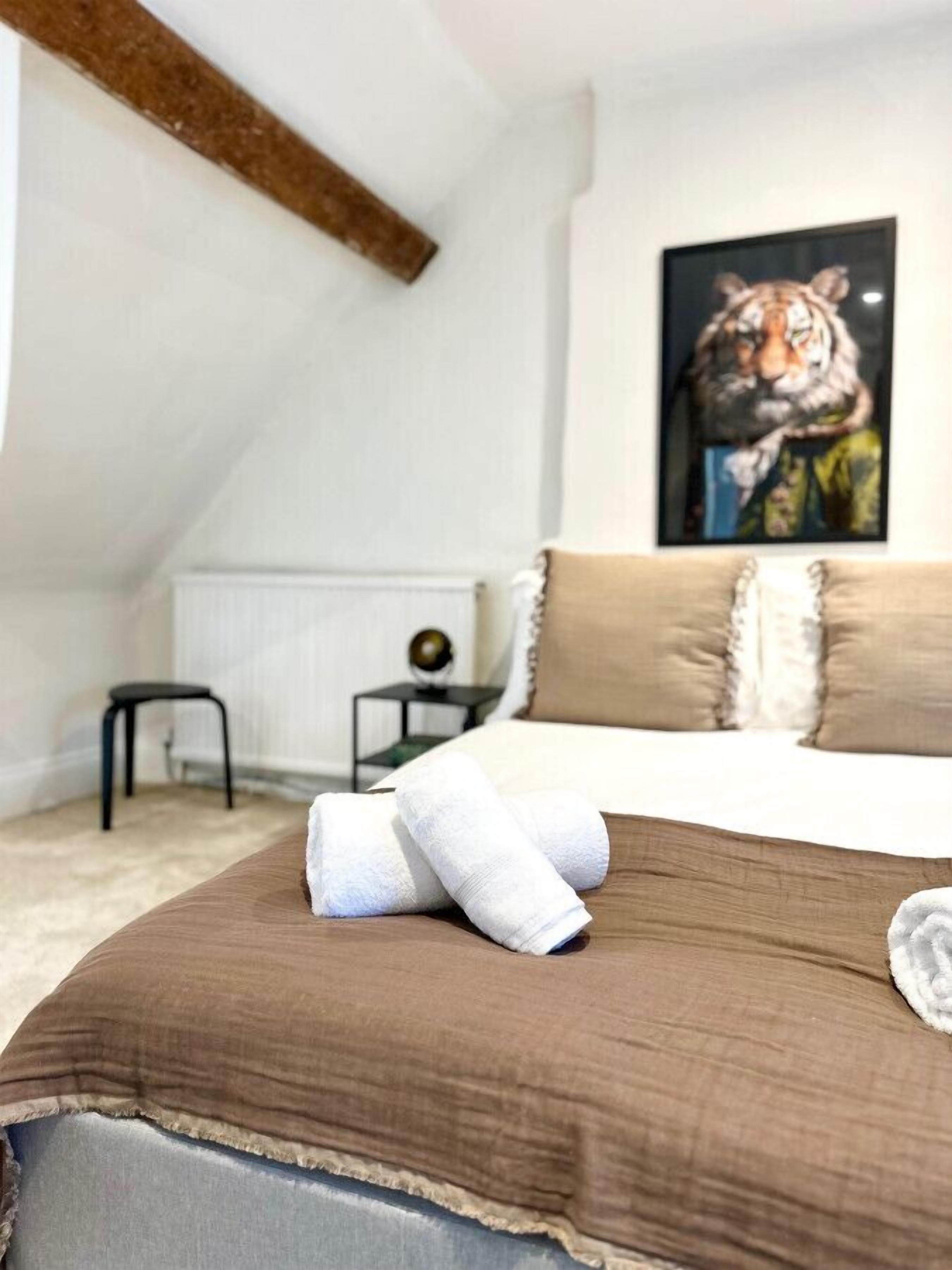 Ett sovrum med ett sluttande tak, en säng med bruna sängkläder, en inramad tavla med ett tigermotiv på väggen och ett litet sidobord med en jordglob.