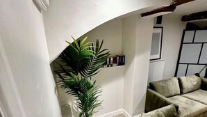 Una sala de estar con un sofá verde, una planta en maceta y suelo de baldosas.