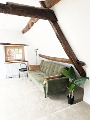 Una stanza in stile loft con travi a vista in legno, un divano verde, un termosifone, una sedia nera e una pianta in vaso.