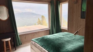Un dormitorio con cama, escritorio y vistas a las montañas a través de amplias ventanas.