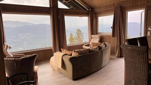 Una habitación acogedora con sofá, sillas y grandes ventanales que ofrecen vistas a la montaña.