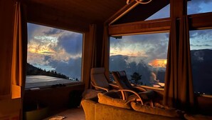 Habitación con vistas a un paisaje montañoso, techo de madera y dos sillones reclinables.