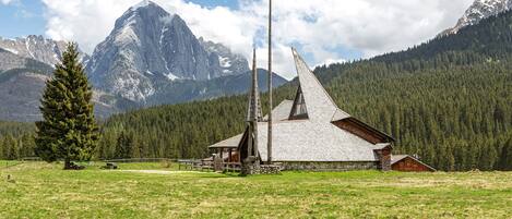 A mountain lodge with a wooden structure, a wooden fence, and a large evergreen tree.