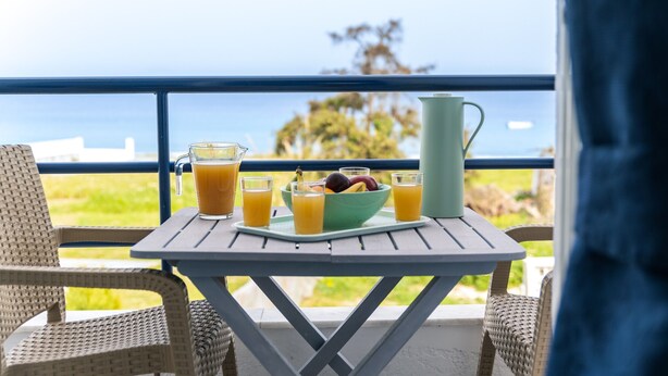 Une table avec un saladier rempli de fruits, des verres de jus d’orange, une carafe et une chaise.