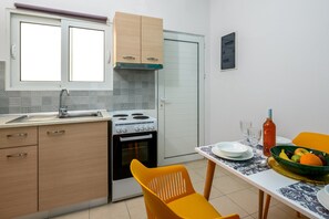 A compact kitchen with a stove, oven, and sink, a dining table with chairs, and a window.