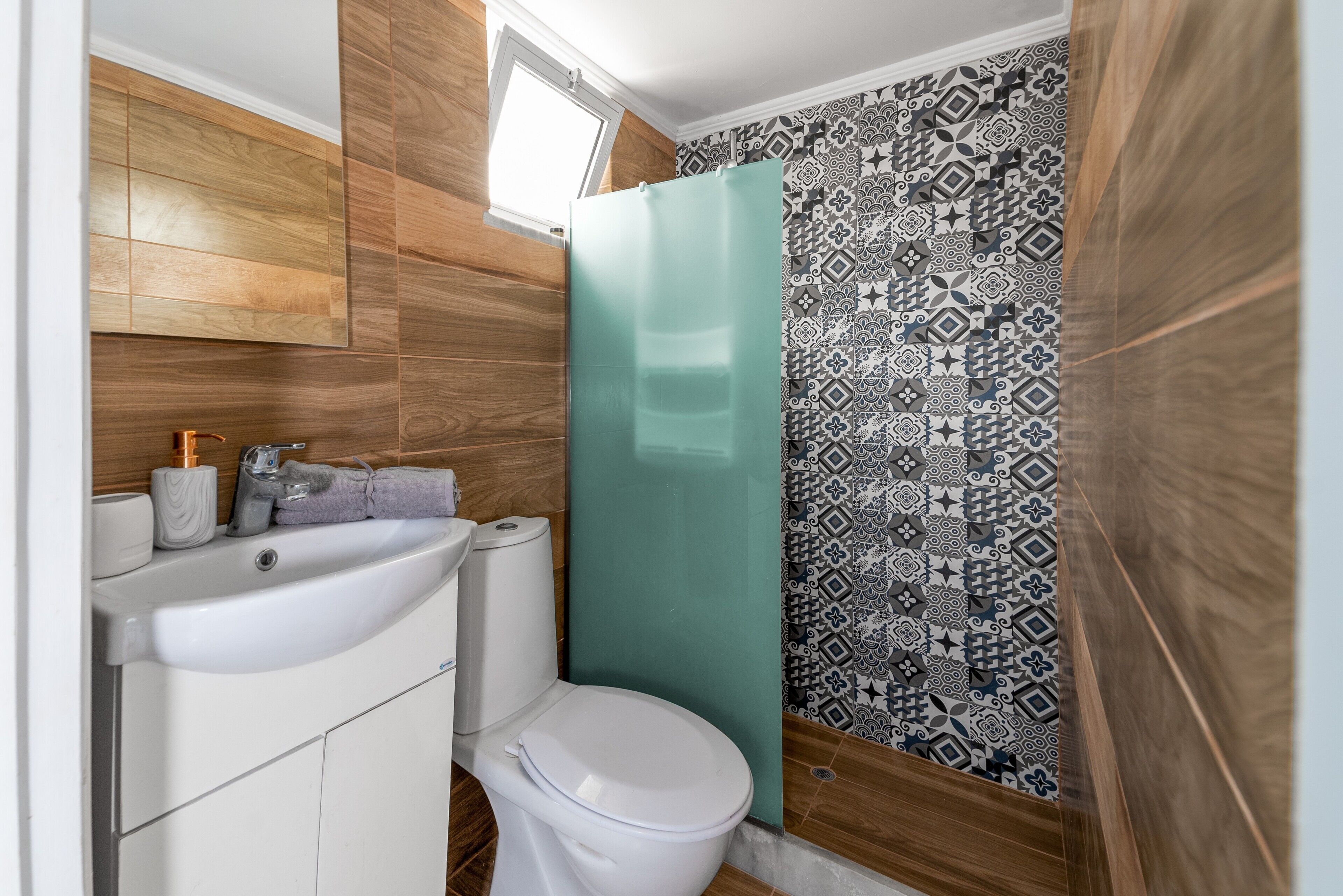 A bathroom with a wooden wall, a patterned shower curtain, a white sink, and a toilet.
