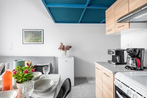 Een moderne keuken met witte apparaten, een blauw plafond en een eethoek met een tafel gedekt voor twee personen.