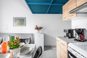 Cozinha moderna com eletrodomésticos brancos, teto azul e área de jantar com mesa posta para dois.