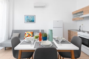 A modern kitchen with a dining area, white appliances, and a colorful cushion on the sofa.