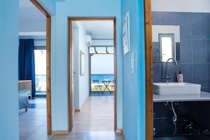 Une chambre moderne avec un plancher en bois, un lavabo blanc et une vue sur la mer depuis un balcon.