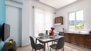 A modern kitchen with wooden cabinets, a dining table with chairs, a TV, and a window with a view of hills. - Apartment 'Rhodes Sea Ialysos' with Balcony, Wi-Fi and Air Conditioning (Ialisos)