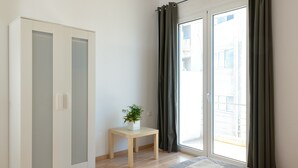 Ein Schlafzimmer mit Bett, Kleiderschrank, einem kleinen Tisch mit Pflanze und Blick durch eine Schiebetür.