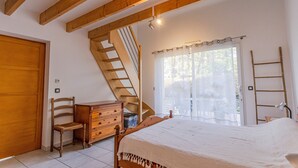 Un dormitorio con una cama y cómoda de madera, una silla, una escalera y una ventana con cortinas.