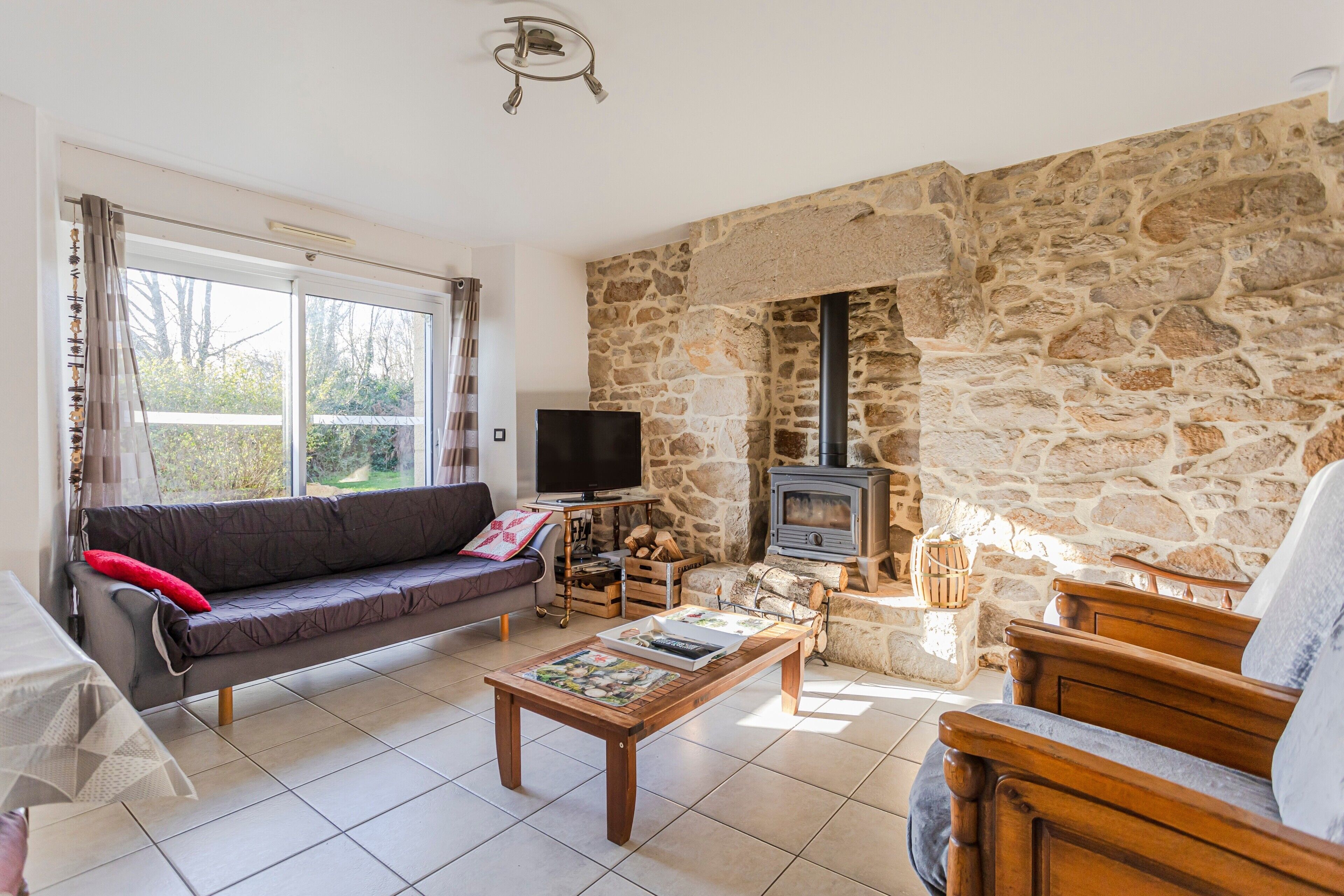 Una sala de estar con pared de piedra, chimenea, sofá, televisor y mesa de centro.