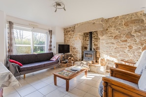 A living room with a stone wall, a fireplace, a sofa, a television, and a coffee table. - Holiday Home 'A La Ferme Du Cosquer' – Accessible, Private Garden & Wi-Fi (Baden)