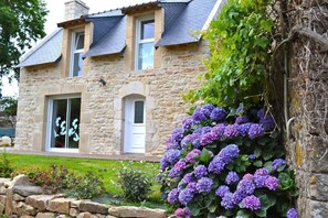 A stone house with a sloped roof, a visible window, and a stone wall with purple hydrangea flowers. - Holiday Home 'A La Ferme Du Cosquer' – Accessible, Private Garden & Wi-Fi (Baden)