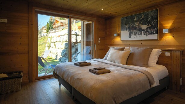 Un dormitorio de cabaña de madera con una cama grande, un vidrio que da al exterior y un cuadro de ciervos en la pared.