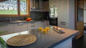 Una cocina moderna con pared de piedra, un ventanal grande y una mesa para el desayuno con zumo de naranja y pasteles.