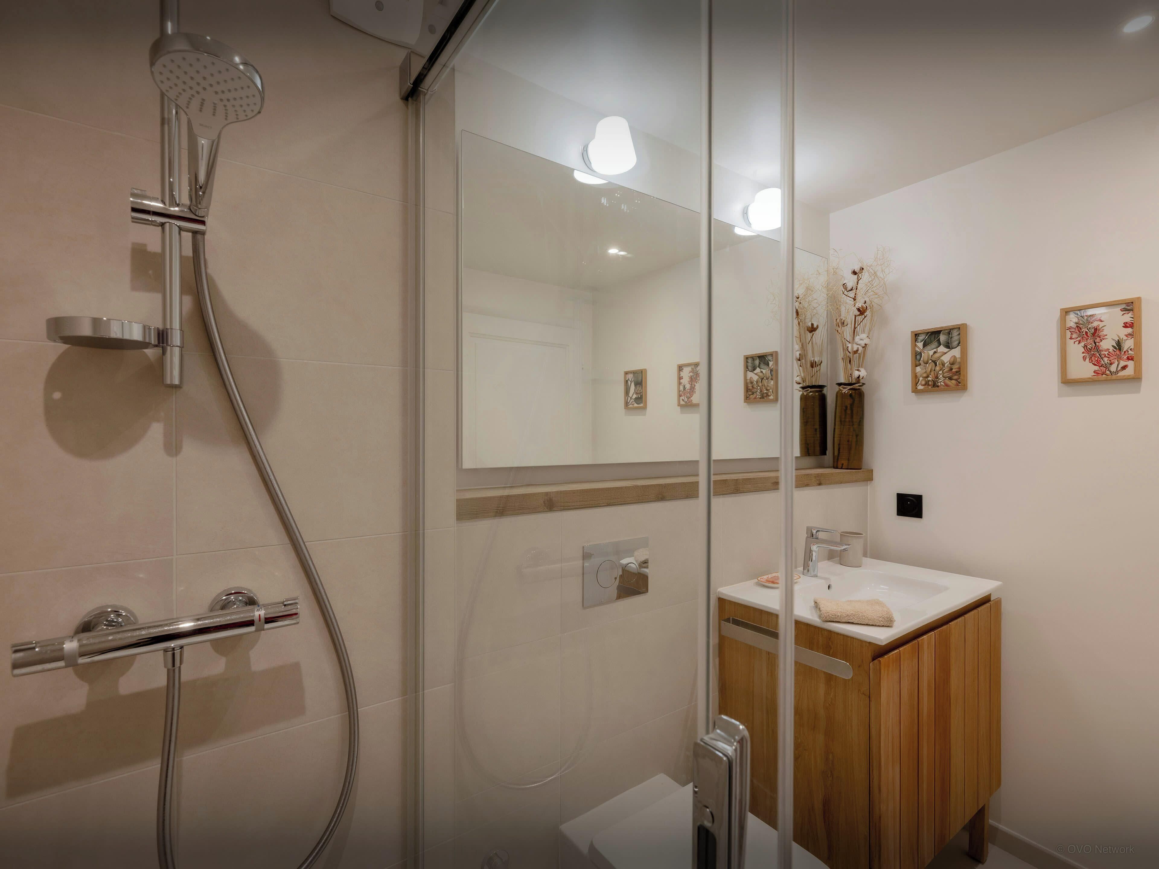 A modern bathroom with a glass shower enclosure, a wooden vanity, and wall-mounted artwork.