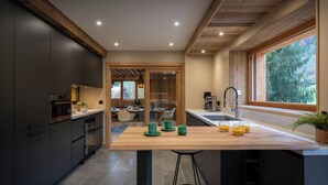 A modern kitchen with dark cabinets, a wooden island, and a view of a dining area.