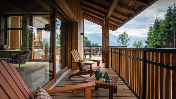 A wooden deck with seating and a table, overlooking a mountainous landscape.
