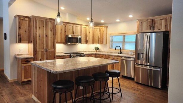 A modern kitchen with wooden cabinets, a stainless steel refrigerator, a microwave, and a large island with bar stools. - Spacious 5-BR home in Manitowish Waters with pier access on Chain of Lakes. (Manitowish Waters)