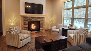 A cozy living room with a stone fireplace, striped furniture, and a large window with a snowy view. - Spacious 5-BR home in Manitowish Waters with pier access on Chain of Lakes. (Manitowish Waters)