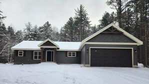 A two-story house with a dark exterior, a garage, and a snow-covered driveway. - Spacious 5-BR home in Manitowish Waters with pier access on Chain of Lakes. (Manitowish Waters)