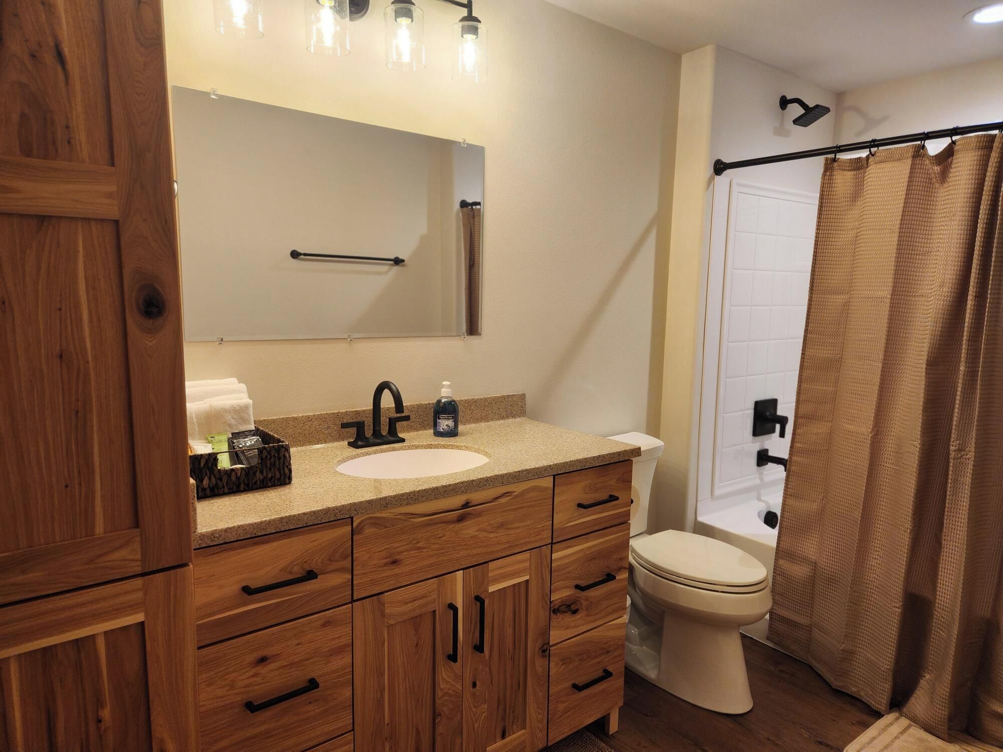 A bathroom with a wooden vanity, a sink, a mirror, a toilet, and a shower curtain.
