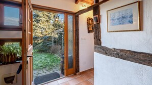 Ein Zimmer mit Holzboden, einer Schiebeglastür, die zu einem Garten führt, einem gerahmten Bild an der Wand und einem Blumentopf auf der Fensterbank.