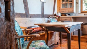 Ein rustikaler Raum mit freiliegenden Holzbalken, einem Holztisch und einem Stuhl mit Blumenkissen.