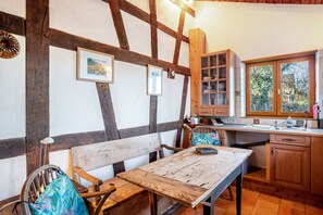 A rustic kitchen with exposed beams, wooden furniture, and a window with a view of trees.