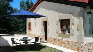 Eine Terrasse mit Tisch und Stühlen, einem blauen Sonnenschirm und einer Steinmauer.