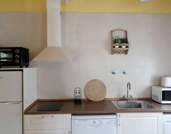 A kitchen with a microwave, toaster, and dishwasher, a sink, and a small shelf with a plant.