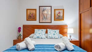 A hotel room with a wooden headboard, a bed with blue and white patterned pillows, a blue bedspread, and two rolled towels on the bed. There are three framed artworks on the wall above the bed. - Apartment 'Mas' with Sea View, Wi-Fi and Air Conditioning (Salou)