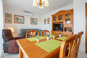 Zona pranzo con tavolo in legno, sedie e pensile TV.