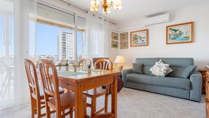 A modern living room with a dining table, wooden chairs, a grey sofa, and a chandelier. - Apartment 'Mas' with Sea View, Wi-Fi and Air Conditioning (Salou)