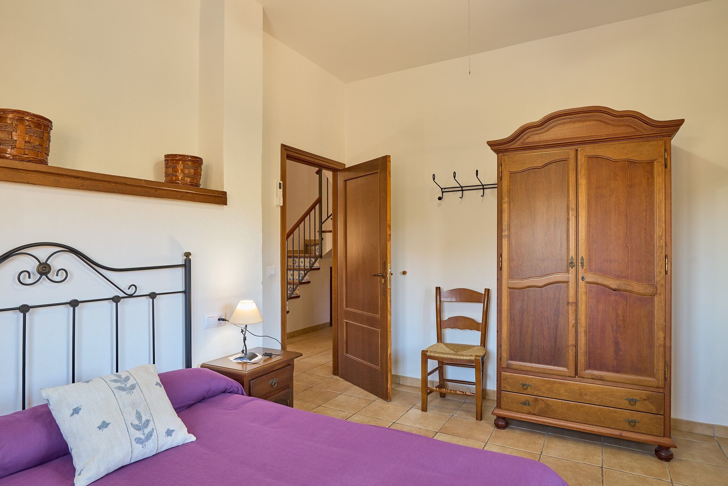 Un dormitorio con cama, mesita de noche, lámpara, armario de madera, silla y una escalera.