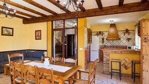 Un comedor con mesa y sillas de madera, una araña y una cocina con salpicadero de azulejos.