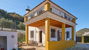 Una casa de dos pisos con un balcón, un patio con sillas y una reja.